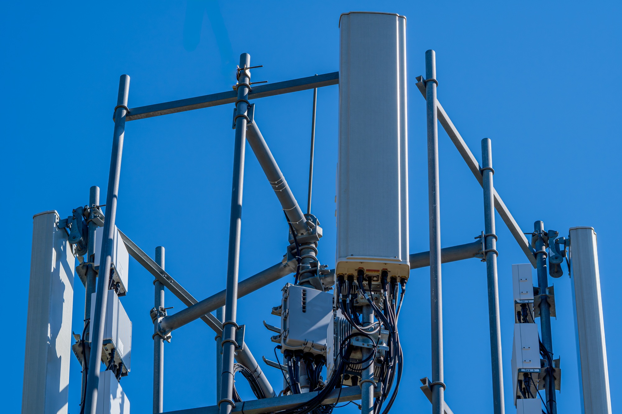 Close-up of tower with 6G, 5G, 4G cellular network antenna on blue sky background.